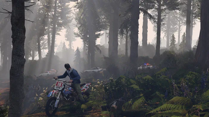 Dans Grand Theft Auto V Legacy, un personnage sur une moto est arrêté dans une forêt brumeuse avec des voitures de police en arrière-plan.