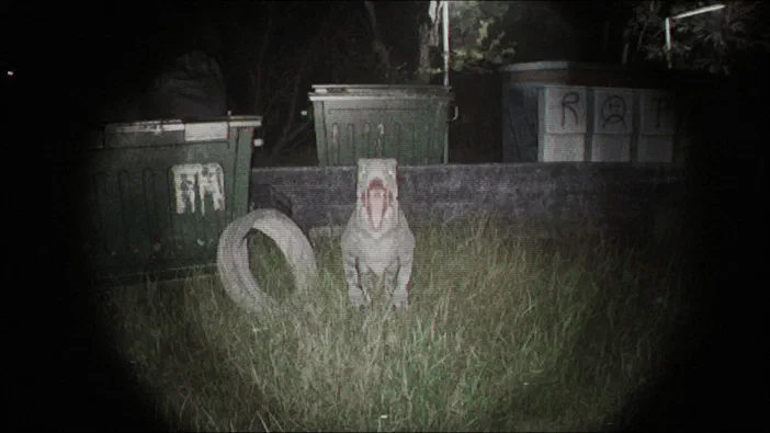 Capture d'écran du jeu Unknown Tapes montrant un personnage blanc avec une bouche rouge ouverte debout dans l'herbe devant des poubelles.