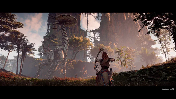 Dans Horizon Zero Dawn™ Complete Edition, une archer rouge chevelure observe un paysage de forêts et falaises avec des structures mécaniques.