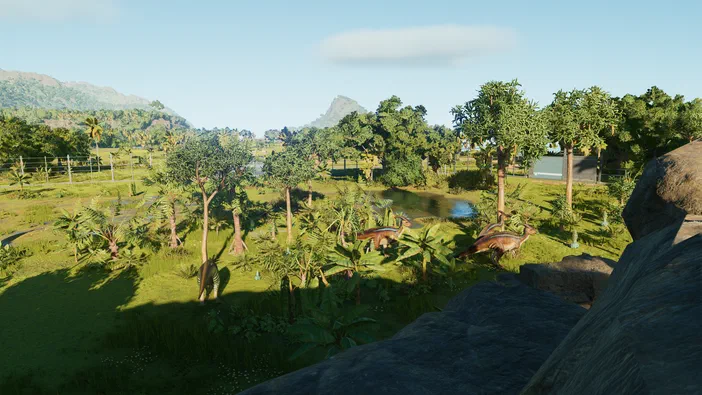 Vue d'un paysage verdoyant dans le jeu Jurassic World Evolution, montrant deux Parasaurolophus près de l'eau et des arbres.