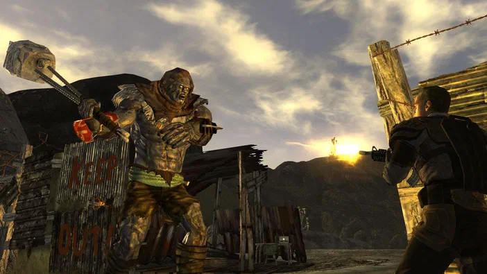 Dans Fallout: New Vegas, un joueur arme son fusil face à une créature musclée tenant une masse près d'une barrière avec l'inscription KEEP OUT au coucher du soleil.