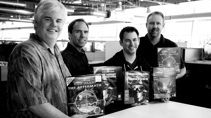 Quatre hommes souriants tenant des boîtes du jeu vidéo Command & Conquer Remastered Collection dans un bureau.