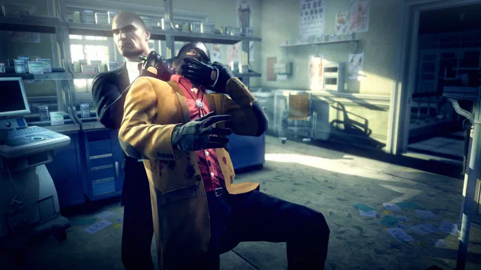 Dans le jeu Hitman: Absolution, un assassin en manteau taché de sang tient une arme sur la gorge d'un homme assis dans un bureau médical.