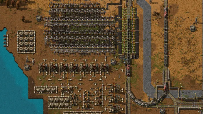 Vue aérienne d'une base industrielle complexe dans le jeu Factorio avec des usines alignées et un réseau de rails.