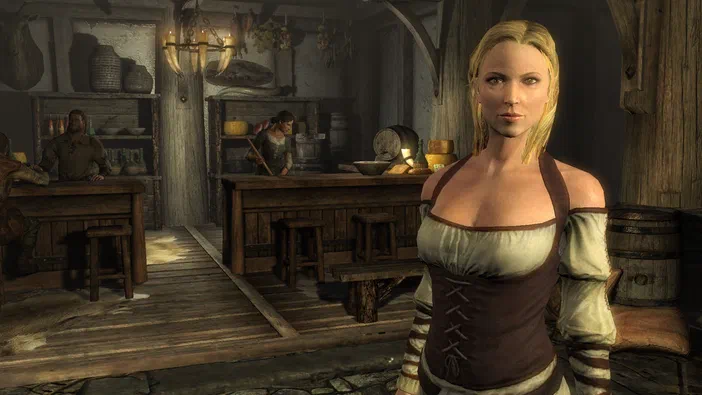 Dans The Elder Scrolls V: Skyrim, une femme blonde en tenue de cuir se tient dans un tavern rustique avec des barreaux et d'autres personnages au fond.