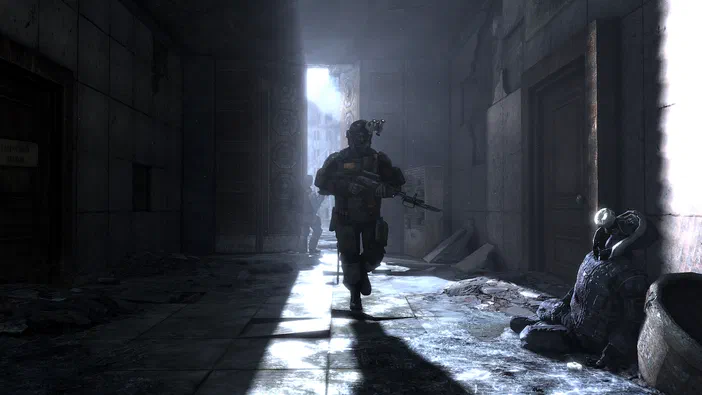 Dans le jeu vidéo Metro 2033, un soldat en armure avance dans un couloir sombre et délabré où gît son camarade blessé.