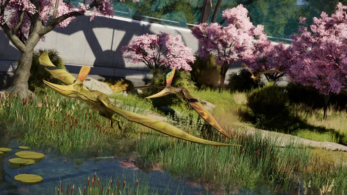 Dans Jurassic World Evolution 3, deux pterosaures aux ailes colorées survolent un étang bordé de roseaux et d'arbres à fleurs roses.