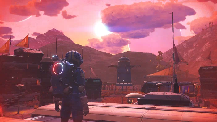 Dans le jeu vidéo No Man's Sky, un astronaute observe une base spatiale sur une planète aux couleurs roses et oranges sous un ciel étoilé.