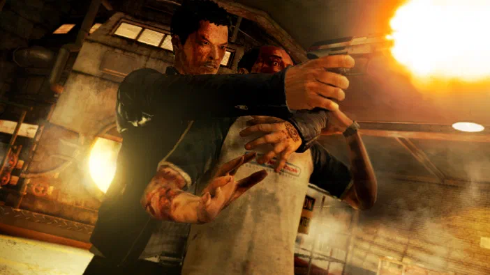 Dans le jeu Sleeping Dogs, un personnage tient une arme à feu enflammée tout en agrippant un autre homme blessé dans un environnement industriel.
