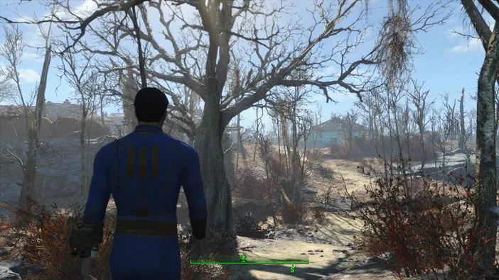 Capture d'écran du jeu Fallout 4 montrant un personnage en combinaison bleue se tenant dans une zone désertique avec des arbres dépouillés et des bâtiments à l'arrière-plan.