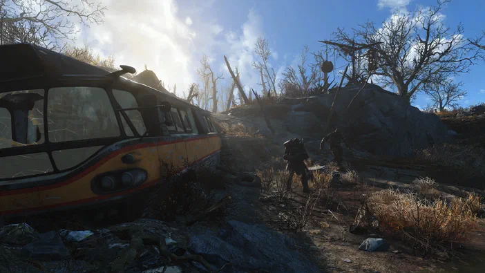 Capture d'écran de Fallout 4 montrant un personnage en armure dans une zone post-apocalyptique avec des débris et un bus abandonné sous un ciel bleu.