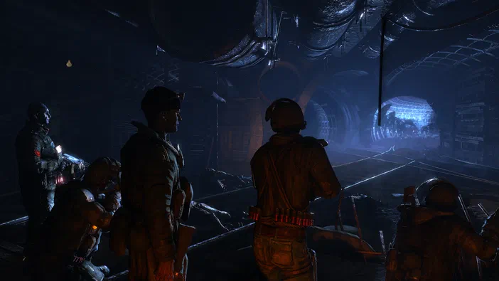 Dans le jeu vidéo Metro 2033, un groupe de soldats en tenue tactique se tient dans une vaste station souterraine aux rails et à l'architecture industrielle sombre.