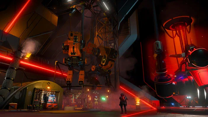 Capture d'écran du jeu vidéo No Man's Sky montrant une base industrielle futuriste avec des robots géants et un personnage en armure dans un environnement aux lumières rouges.