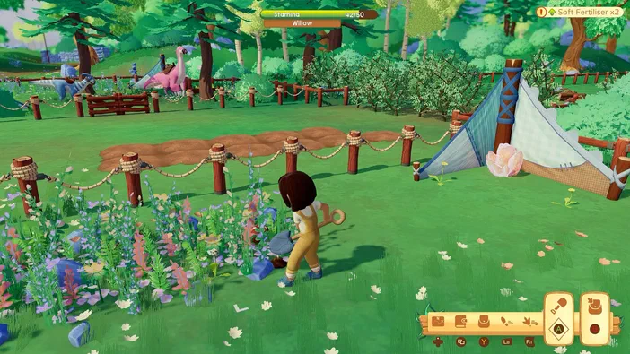 Dans le jeu Paleo Pines, un personnage récolte des plantes dans une clairière verdoyante bordée de clôtures en bois et d'animaux colorés.