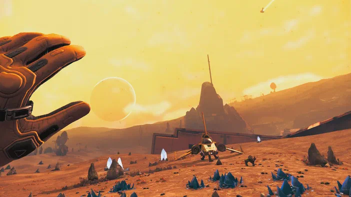Capture d'écran du jeu vidéo No Man's Sky montrant une main gantée devant un paysage désertique avec des cristaux bleus et une planète en arrière-plan.