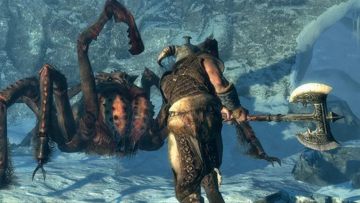 Dans The Elder Scrolls V: Skyrim, un guerrier en armure tenant une hache affronte un grand arachnide dans une grotte enneigée.