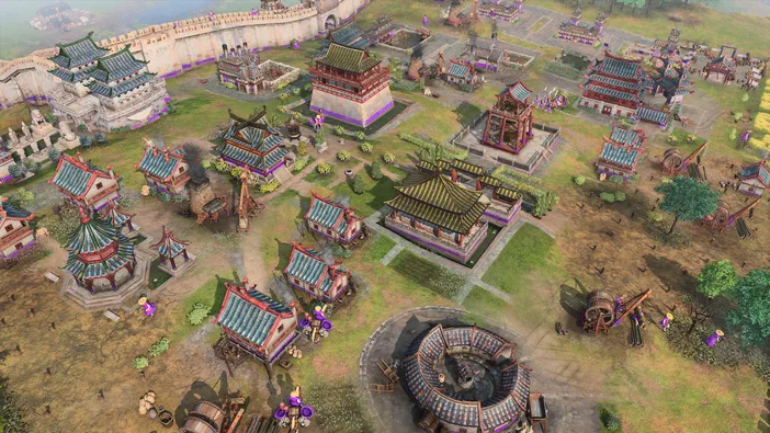 Vue aérienne d'une ville médiévale dans Age of Empires IV avec des bâtiments en bois et pierre, une muraille fortifiée et des unités militaires.