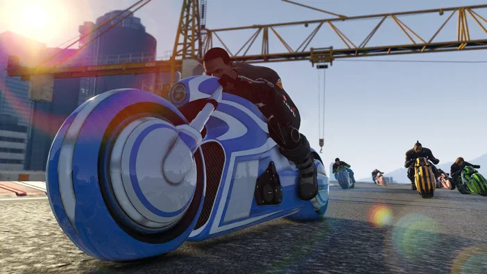 Dans Grand Theft Auto V Legacy, un personnage pilote une moto futuriste bleue et blanche sur une route ensoleillée avec d'autres motos au loin.