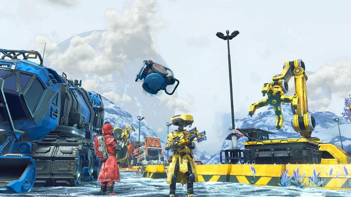 Dans le jeu vidéo No Man's Sky, deux personnages en combinaisons colorées se tiennent près d'un véhicule bleu et d'une structure jaune avec un bras robotique dans une zone enneigée.