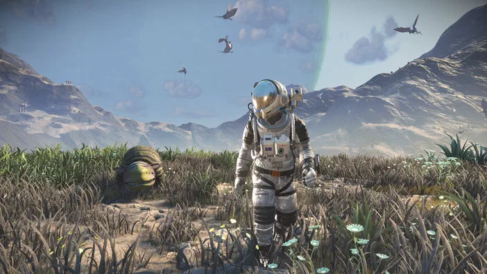 Dans le jeu vidéo No Man's Sky, un astronaute marche sur une planète aux champs de fleurs bleues avec des créatures ailées en arrière-plan.