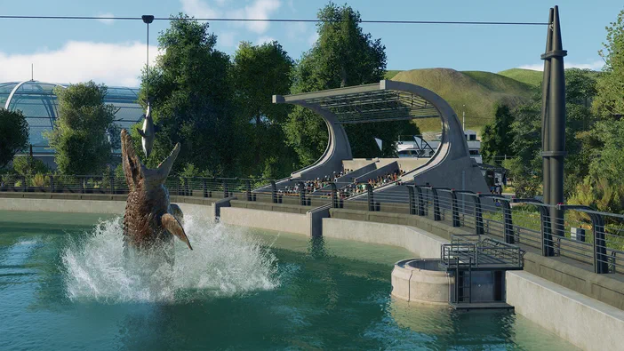 Dans Jurassic World Evolution 2, un dinosaure saute hors de l'eau dans une aire d'exposition avec des visiteurs.