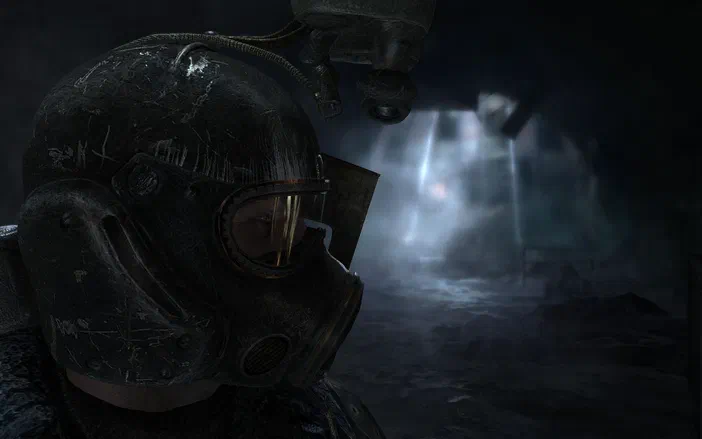 Dans le jeu vidéo Metro 2033, un personnage en combinaison de protection se tient dans une grotte sombre éclairée par des rayons lumineux.