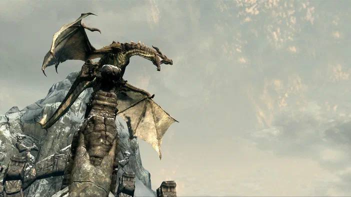 Capture d'écran du jeu vidéo The Elder Scrolls V: Skyrim montrant un dragon perché sur une structure en pierre dans un paysage montagneux sous un ciel nuageux.