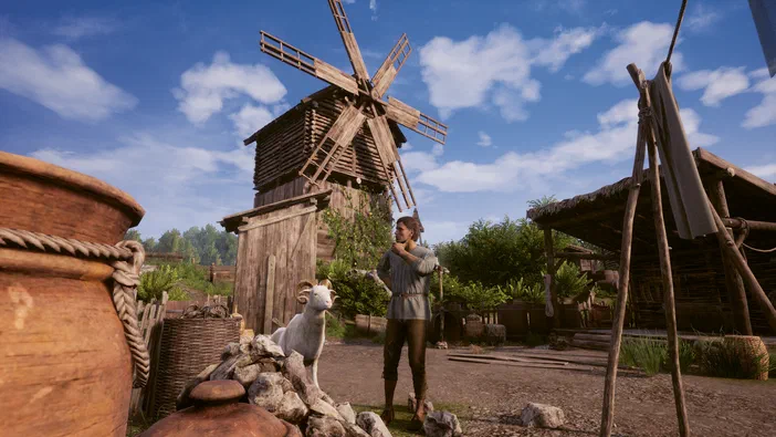 Dans le jeu vidéo Medieval Dynasty, un personnage se tient dans une cour de ferme avec des jarres et une chèvre blanche devant lui. Un moulin à vent en bois est visible au fond sous un ciel bleu.