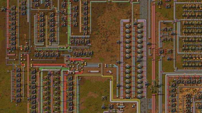 Vue de dessus d'une base complexe dans le jeu Factorio avec des rangées de machines et un réseau dense de tuyaux colorés.