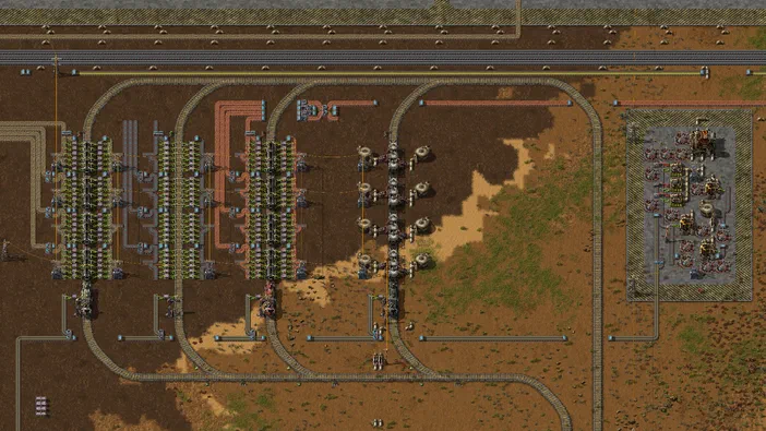 Vue de dessus d'une base complexe dans le jeu Factorio avec des lignes de production et des rails.