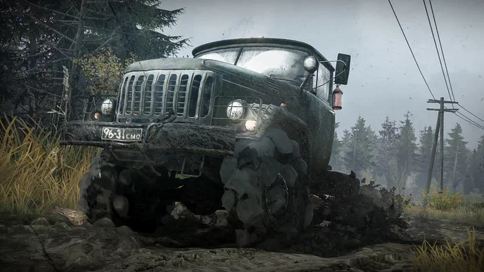 Sous le jeu MudRunner : un camion tout-terrain recouvert de boue traverse une zone marécageuse avec des arbres en arrière-plan.