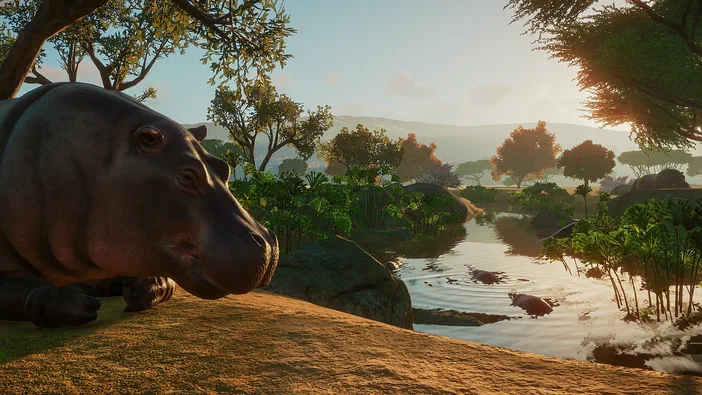 Dans le jeu Planet Zoo, un hippopotame repose sur une berge herbeuse au bord d'une rivière ensoleillée.