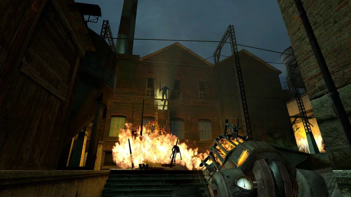 Capture d'écran de Half-Life 2 montrant une arme à la première personne face à un incendie dans une cour industrielle avec des ennemis.