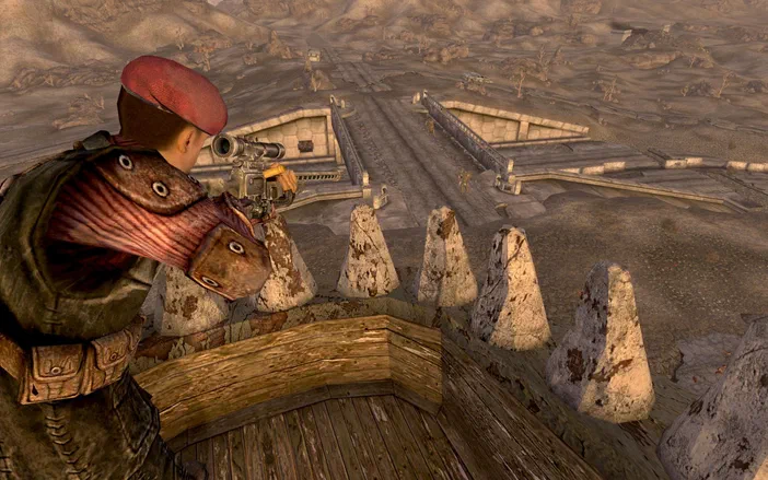 Dans Fallout: New Vegas, un personnage en tenue de combat observe une base désertique depuis une plateforme surélevée.