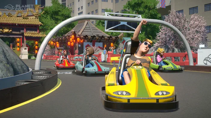 Capture d'écran du jeu Planet Coaster montrant des personnages dans des go-karts colorés sur une piste de course avec un décor asiatique.