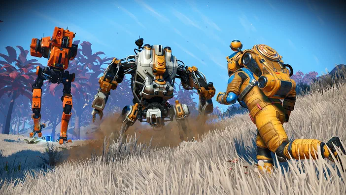Dans le jeu vidéo No Man's Sky, un personnage en combinaison jaune se tient à côté de deux robots orange et gris sur une colline herbeuse sous un ciel bleu.