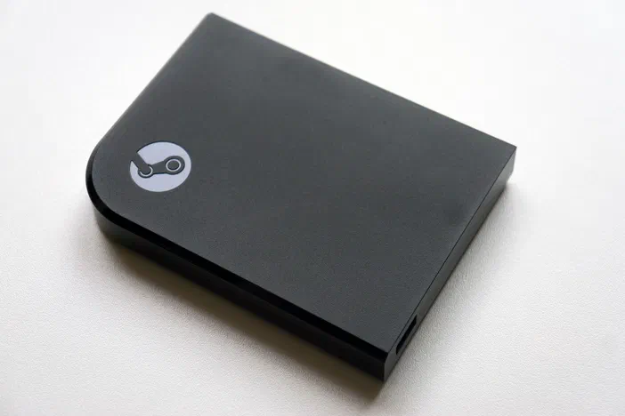 Le boitier Steam Link noir avec le logo circulaire blanc sur la face avant.