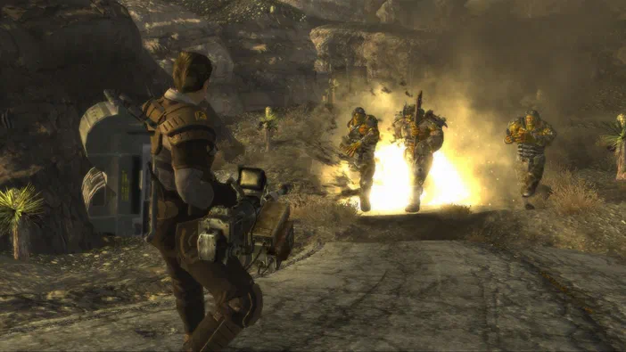 Capture d'écran de Fallout: New Vegas montrant un personnage armé face à trois ennemis dans une zone désertique avec des explosions.