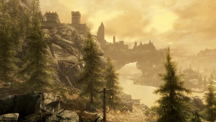 Vue du jeu The Elder Scrolls V: Skyrim Special Edition montrant un château sur une falaise, des arbres et un pont en pierre sous un ciel jaune.