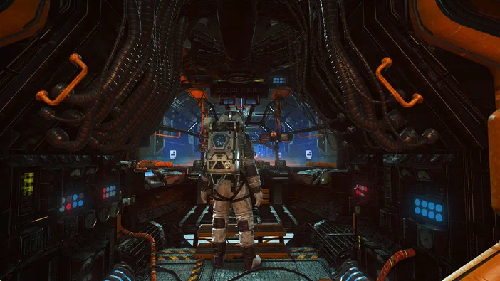 Vue depuis l'intérieur d'un vaisseau spatial dans le jeu No Man's Sky. Un personnage en combinaison spatiale se tient au centre sur une plateforme métallique, entouré de conduits et de panneaux lumineux bleus.
