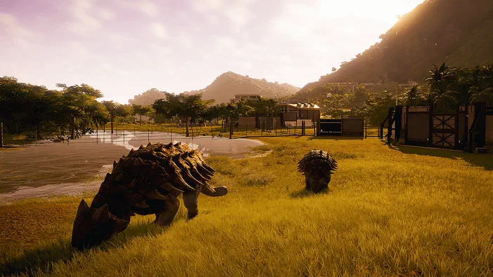Deux dinosaures herbivores broutent dans un parc verdoyant sous le soleil couchant du jeu Jurassic World Evolution.