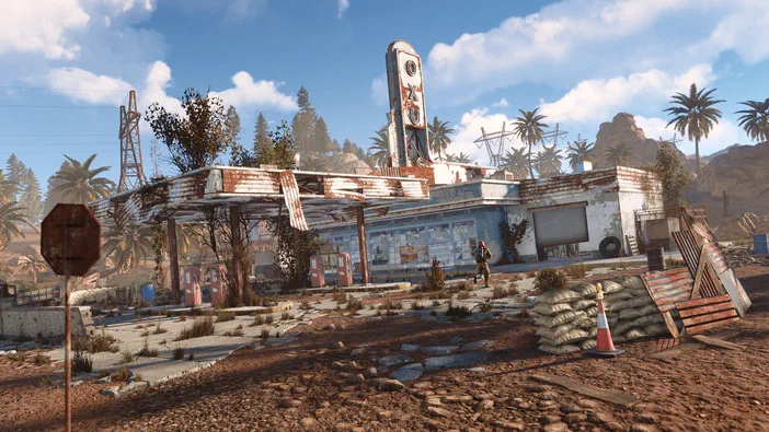 Capture d'écran du jeu Rust montrant une base abandonnée en ruine dans un paysage désertique avec des palmiers et un personnage à proximité.