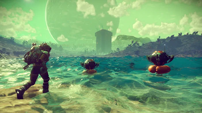 Dans le jeu vidéo No Man's Sky, un personnage en combinaison spatiale marche sur une plage sablonneuse où deux petits robots flottent dans l'eau turquoise sous un ciel vert avec une planète géante.