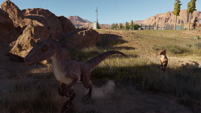 Dans Jurassic World Evolution, un dinosaure à plumes court sur une plage rocheuse avec d'autres dinos en arrière-plan.