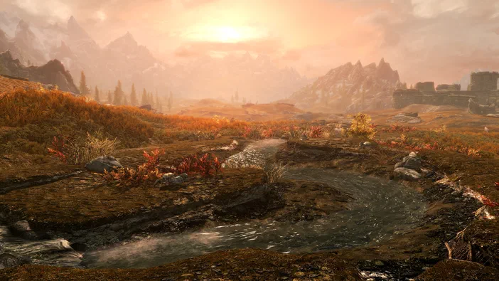 Paysage de Skyrim au coucher du soleil avec une rivière serpentant à travers des collines herbeuses et des montagnes lointaines.