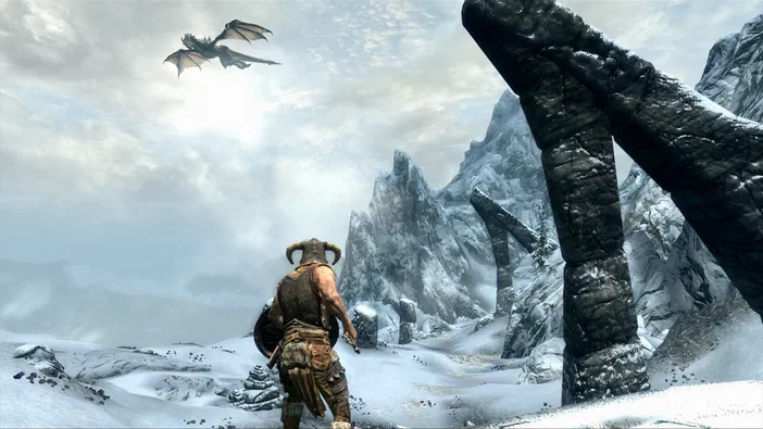 Dans The Elder Scrolls V: Skyrim, un personnage en armure observe une créature ailée voler au-dessus d'un paysage enneigé avec des formations rocheuses.