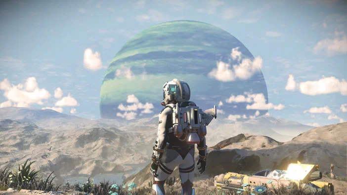 Dans le jeu vidéo No Man's Sky, un astronaute observe une planète verte et bleue depuis des montagnes arides sous un ciel nuageux.